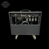 The rear view of a black Fender amplifier with its cabinet door swung open, showing the complex control panel, multiple output tubes, and internal components. The amp is mounted on white caster wheels and photographed against a solid black background.