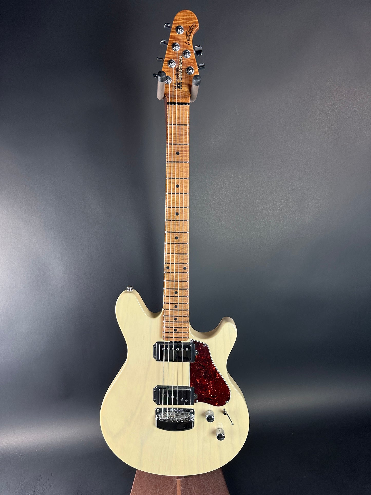 Electric guitar with a cream-colored body and red pickguard on a dark gray background