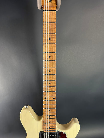 Electric guitar with a beige body and wooden neck on a dark gray background