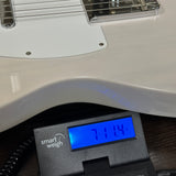A close-up of a white electric bass guitar body resting on a digital smart weigh scale displaying 714 lbs.