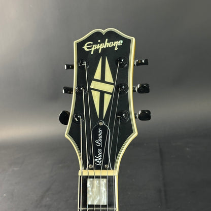 Close-up of a guitar headstock with 'Epiphone' branding on a gray background