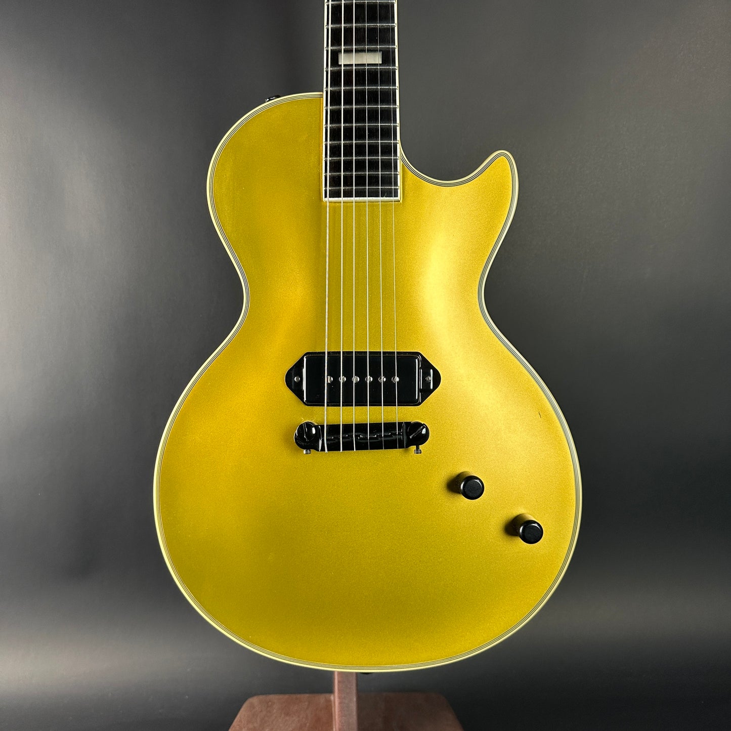 Gold electric guitar on a stand against a dark background