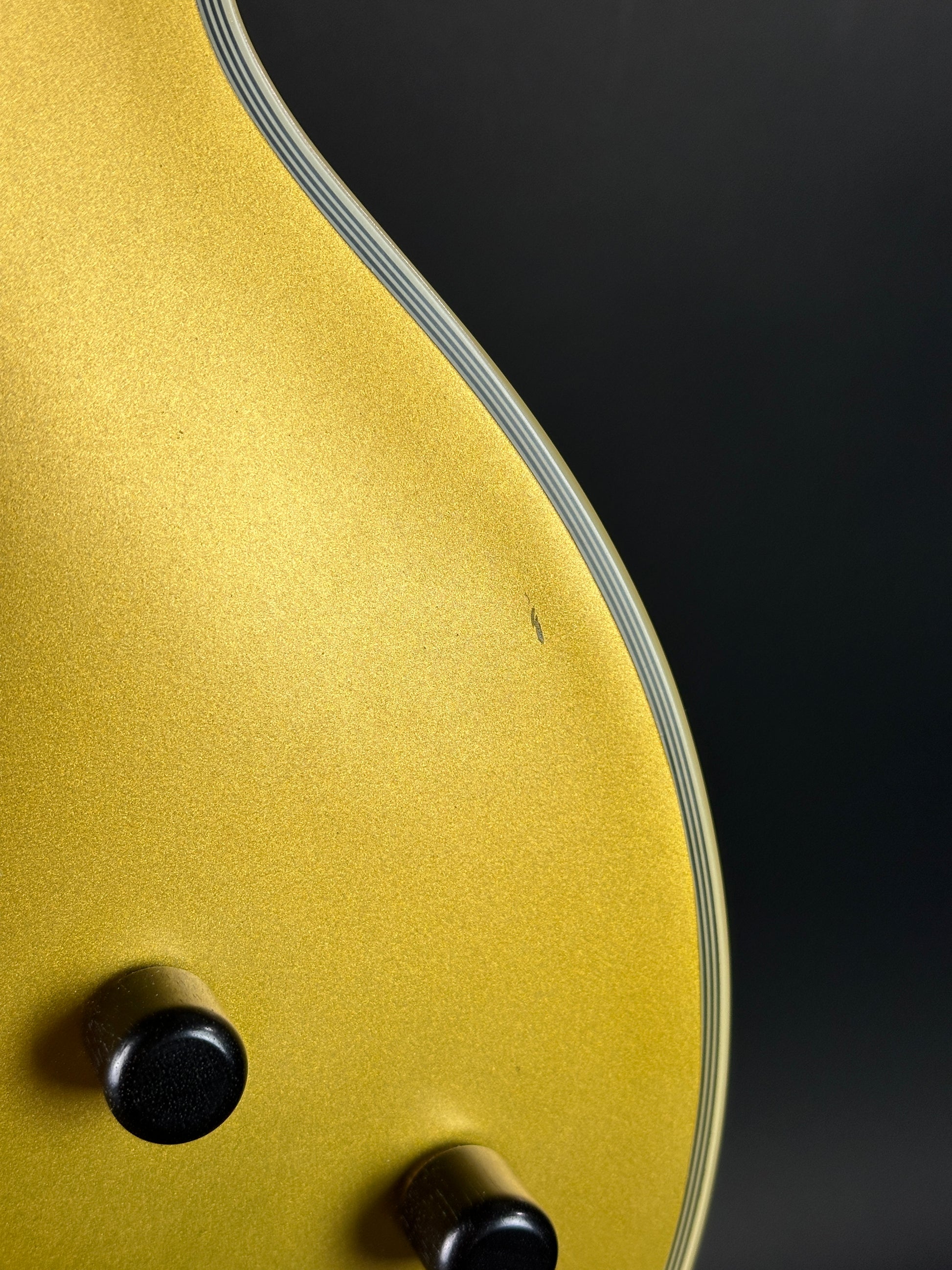Close-up of a gold guitar body with black hardware on a dark background