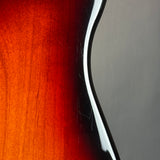 Close-up detail of a glossy dark wood instrument body, showing a warm red-orange sunburst gradient and a white edge trim against a gray background.
