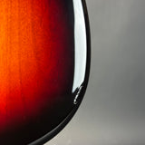 Close-up of a glossy sunburst electric guitar body showing the red and black fade, with a white reflection on the glossy finish against a gray background.