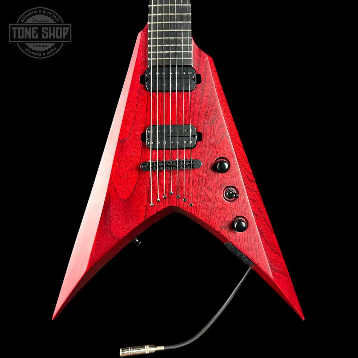 A red electric guitar with a sharp, angular V-shaped body, shown against a solid black background. The guitar features black hardware, pickups, and control knobs, and a black cable is attached at the bottom.