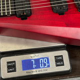 A red electric guitar body and pickups resting on a digital scale showing a weight of 7.09 oz.
