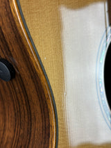 Close-up detail of an acoustic guitar showing the natural wood body, soundhole rosette, and part of the black pickguard.