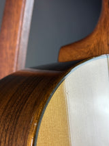 Close-up detail of an acoustic guitar showing the wooden body, sound hole surround, and light-colored top.
