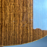 Close-up of a curved wooden surface with a rich, dark brown flamed wood grain pattern and a glossy finish reflecting a blue sky.