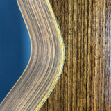 Close-up of a curved wooden object, showing a layered wood grain finish with a dark blue background visible on the left.