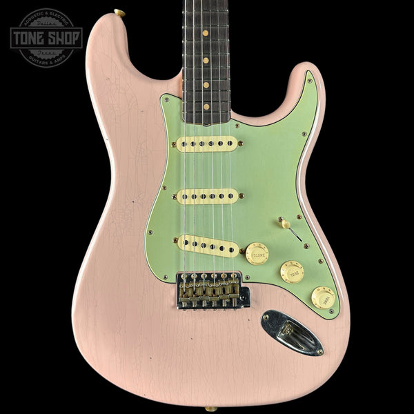 Electric guitar with a green pickguard and pink body on a black background