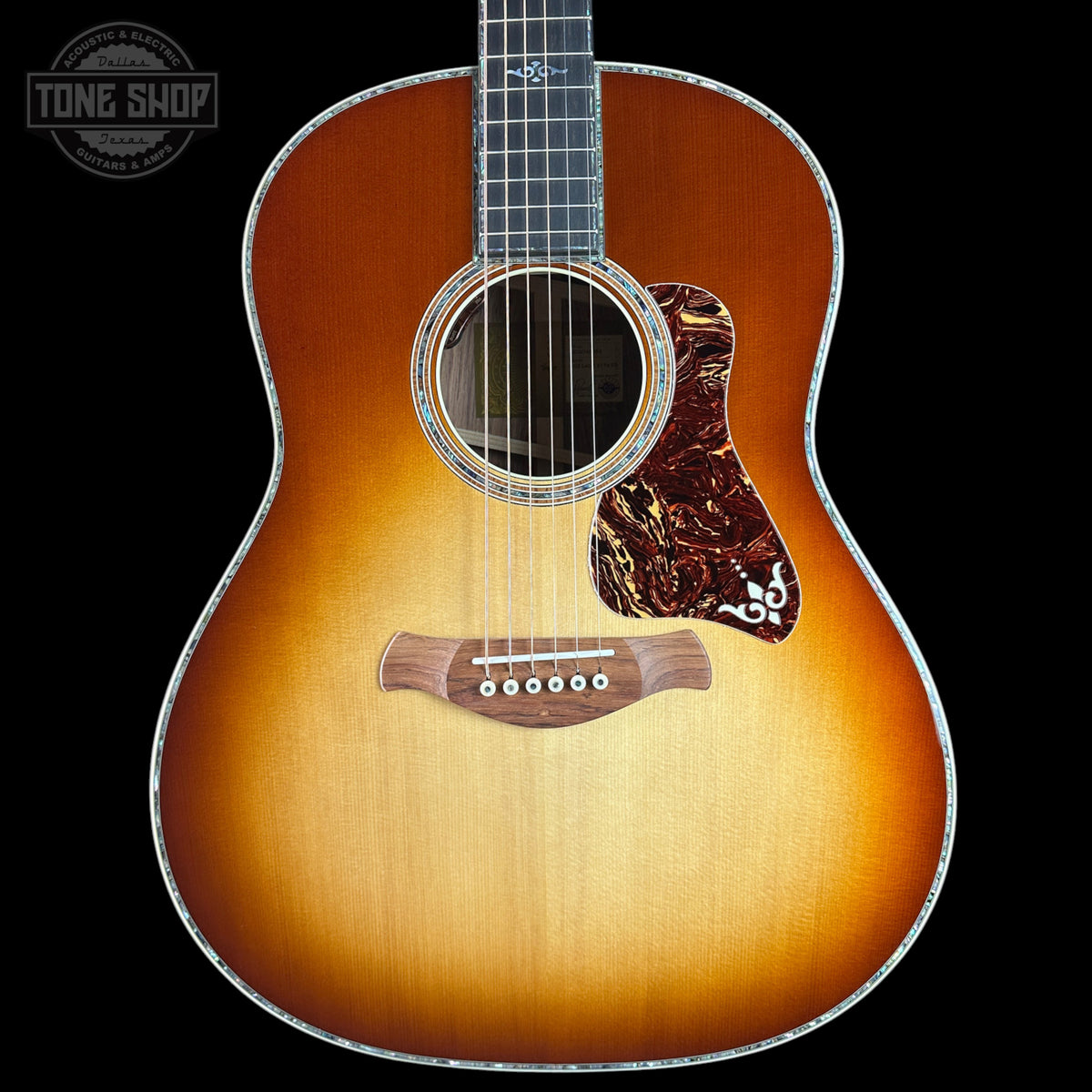 A Taylor acoustic guitar with a classic sunburst finish, featuring a warm orange and brown gradient on a black background. The brand logo is visible on the headstock (partially cropped) and the fretboard, and a 'TONE SHOP' watermark is in the top-left corner.