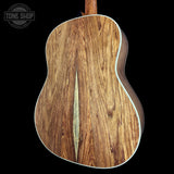 Close-up of the back of an acoustic guitar showing a rich wood grain finish with a central inlay, set against a solid black background with a Tone Shop watermark in the top left.