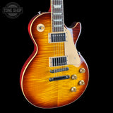 A classic electric guitar with a sunburst finish, featuring a flamed maple top, cream pickguard, and gold hardware, shown against a solid black background.