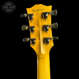 Close-up of the headstock of a yellow Gibson electric guitar against a black background, showing six tuning pegs and the model code CS 601501. A Tone Shop watermark is visible in the top left corner.