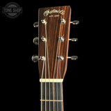Close-up of the headstock of a Martin & Co acoustic guitar against a black background, showing the brand name in gold script, six tuning pegs, and part of the dark wood fretboard.