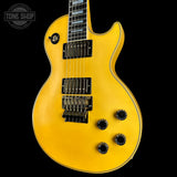A yellow electric guitar with black hardware and control knobs, photographed against a solid black background. A Tone Shop watermark is visible in the top-left corner.