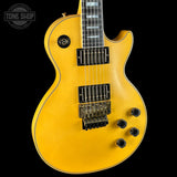 A close-up of a yellow electric guitar body against a black background, showing the glossy finish, black hardware, and control knobs. A Tone Shop watermark is visible in the top left corner.