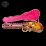 A gold-top electric guitar resting inside an open vintage-style hard case with a bright pink velvet interior, shown against a solid black background. A Tone Shop watermark is visible in the top-left corner.