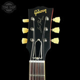 Close-up of a Gibson Les Paul Custom acoustic guitar headstock, featuring a black finish, gold Gibson logo, 'Les Paul Custom' script, and six cream-colored tuning pegs against a black background.