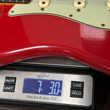 Red electric guitar on a digital scale displaying weight.