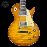 A classic electric guitar with a natural flamed maple top, cream pickguard, and gold hardware, shown against a solid black background. A Tone Shop watermark is visible in the upper left corner.