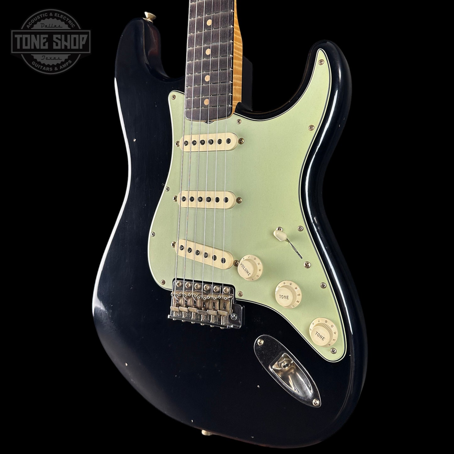 Black electric guitar with a light green pickguard on a black background, featuring 'Tone Shop' logo.