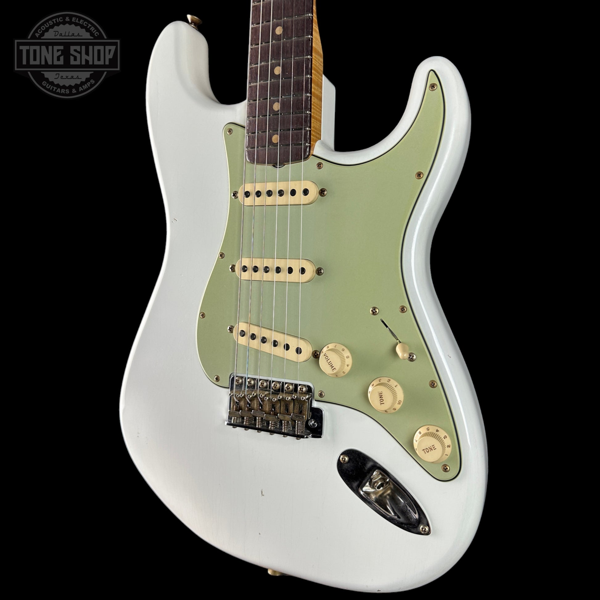 White electric guitar with green pickguard on a black background, featuring 'Tone Shop' logo.
