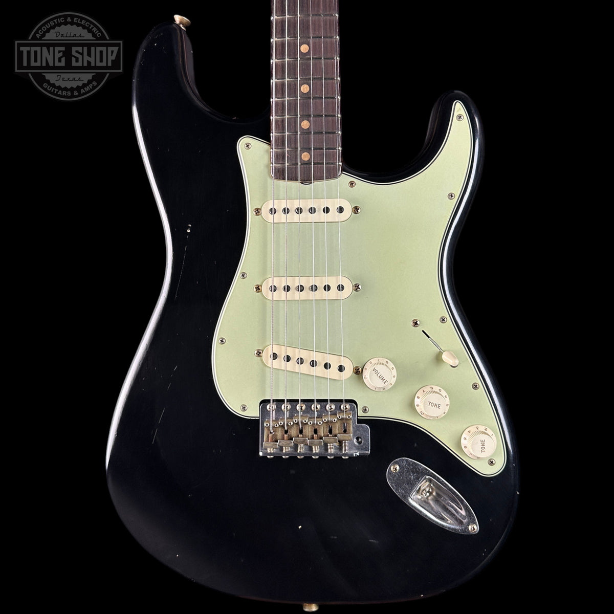 Black electric guitar with a light green pickguard on a black background, featuring 'Tone Shop' branding.
