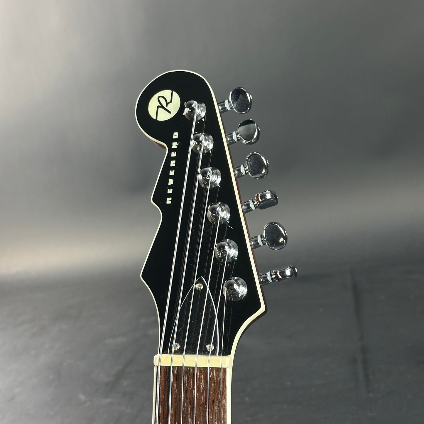 Close-up of a guitar headstock with tuning pegs on a dark background