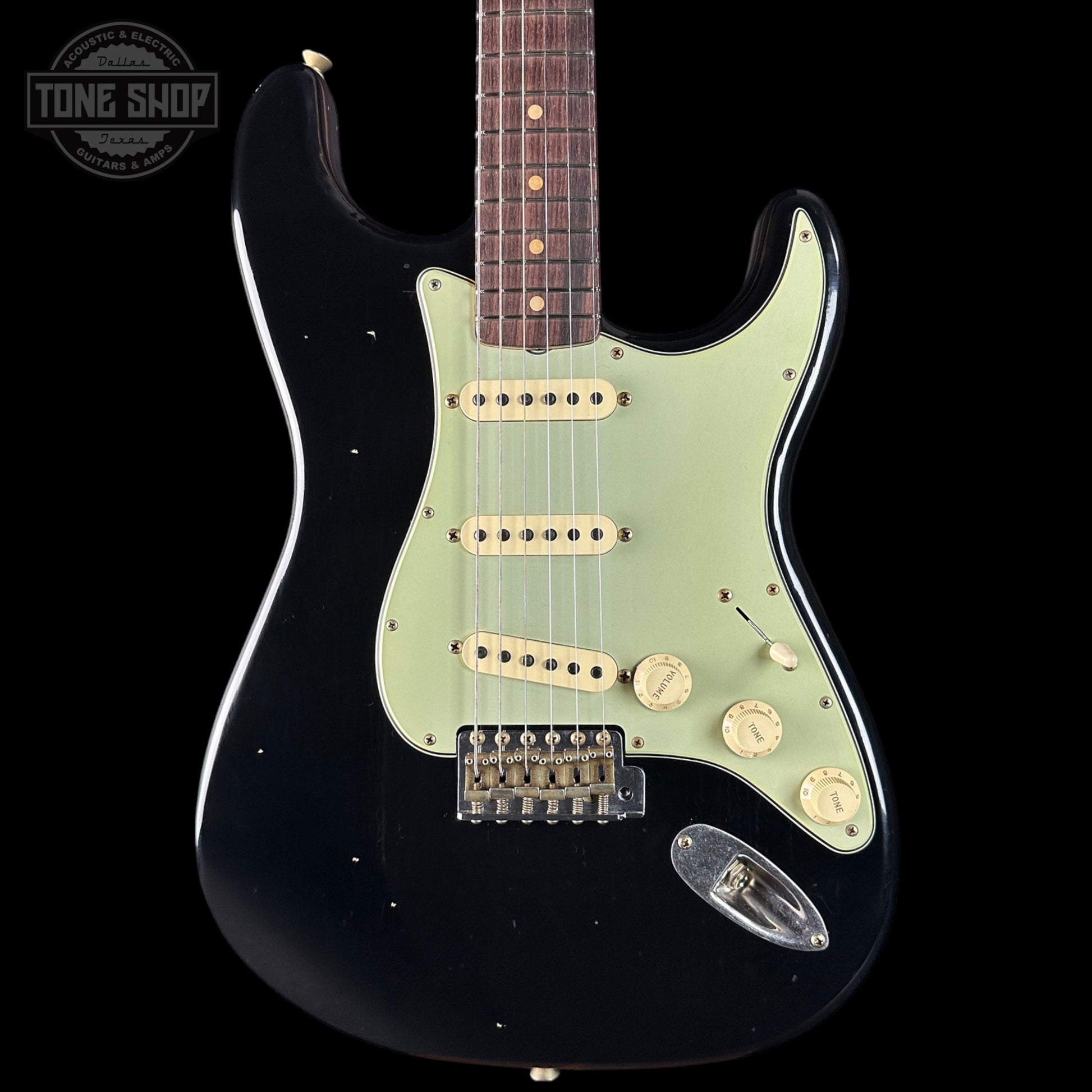 Black electric guitar with a light green pickguard on a black background, featuring 'Tone Shop' branding.