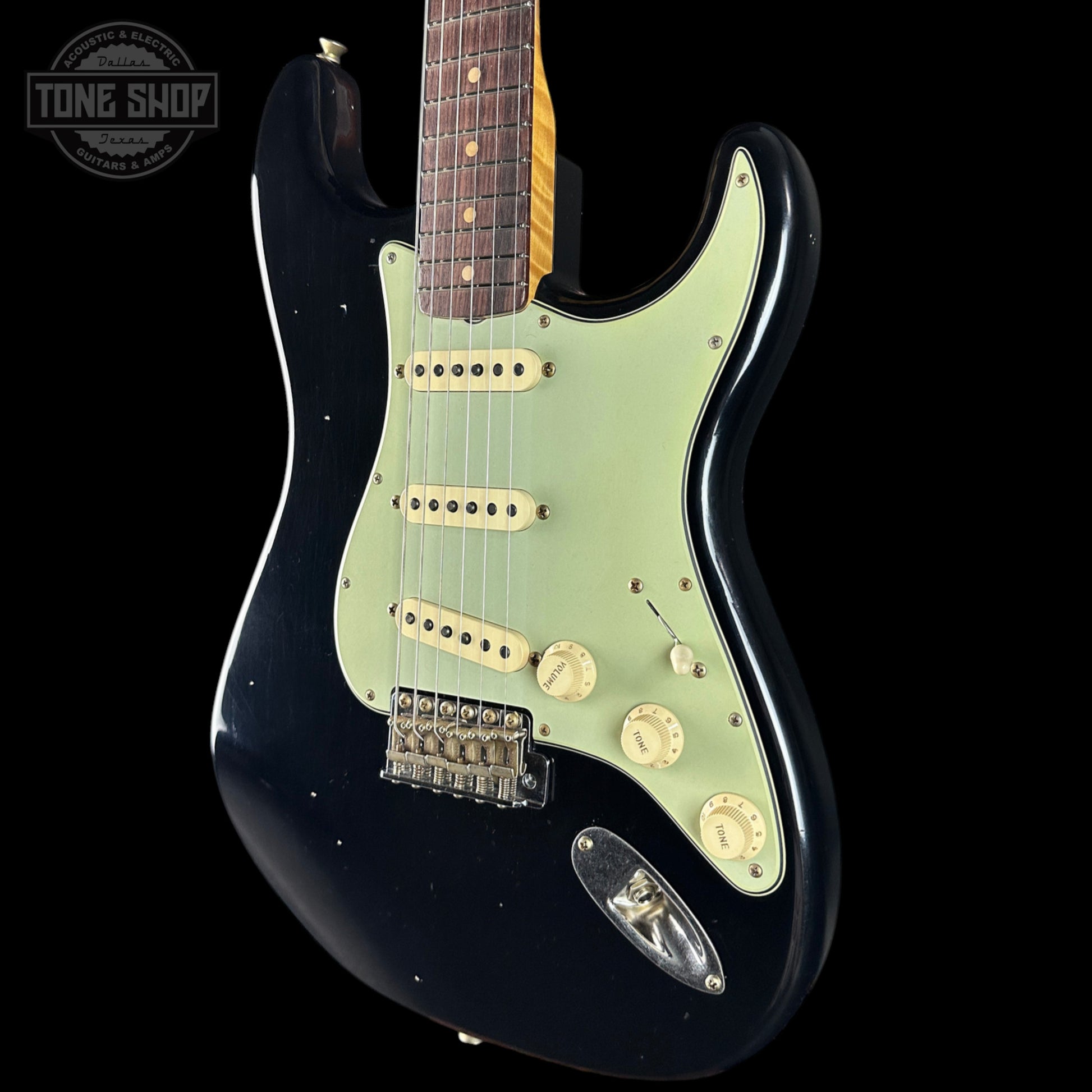 Black electric guitar with a light green pickguard on a black background, featuring 'Tone Shop' logo.