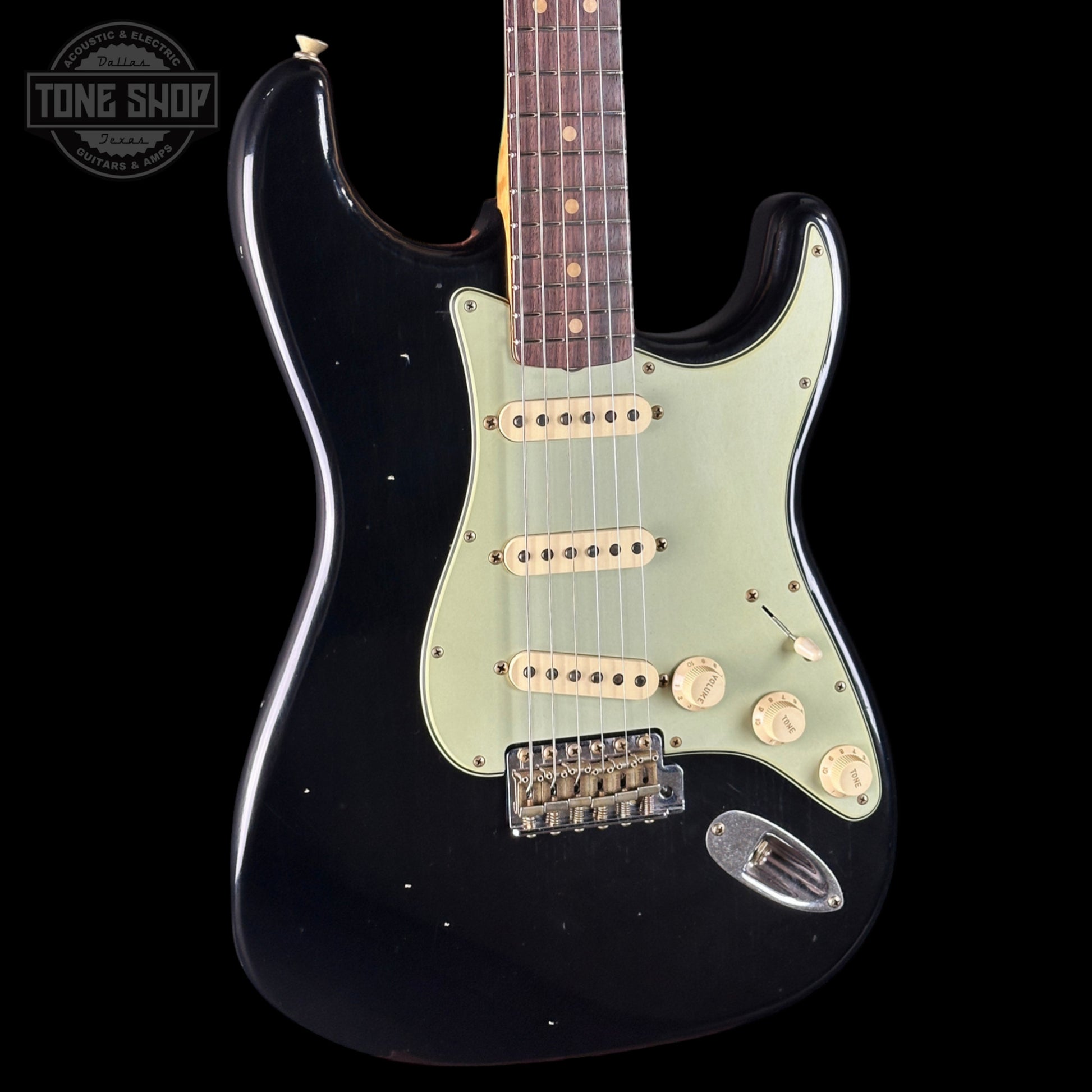 Black electric guitar with a light green pickguard on a black background, featuring 'Tone Shop' branding.