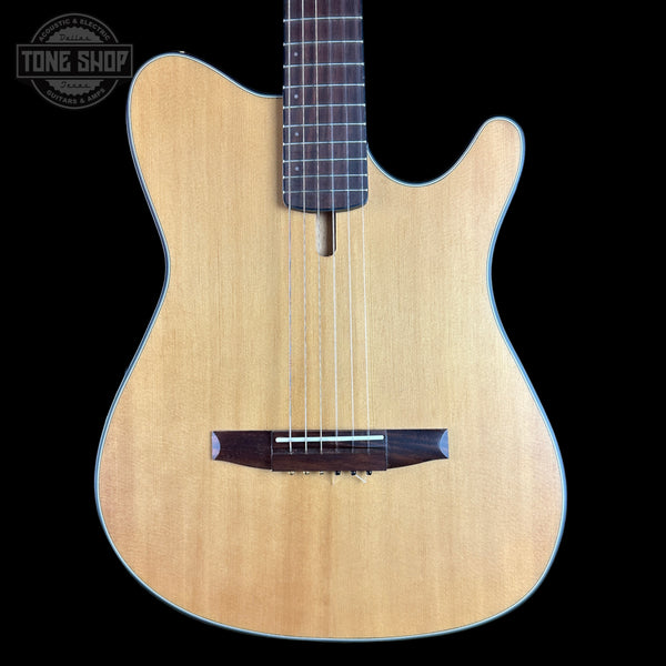 A close-up of a wooden electric guitar body with a natural light wood finish, dark brown bridge and headstock area, and a black background. A Tone Shop watermark is visible in the top left corner.