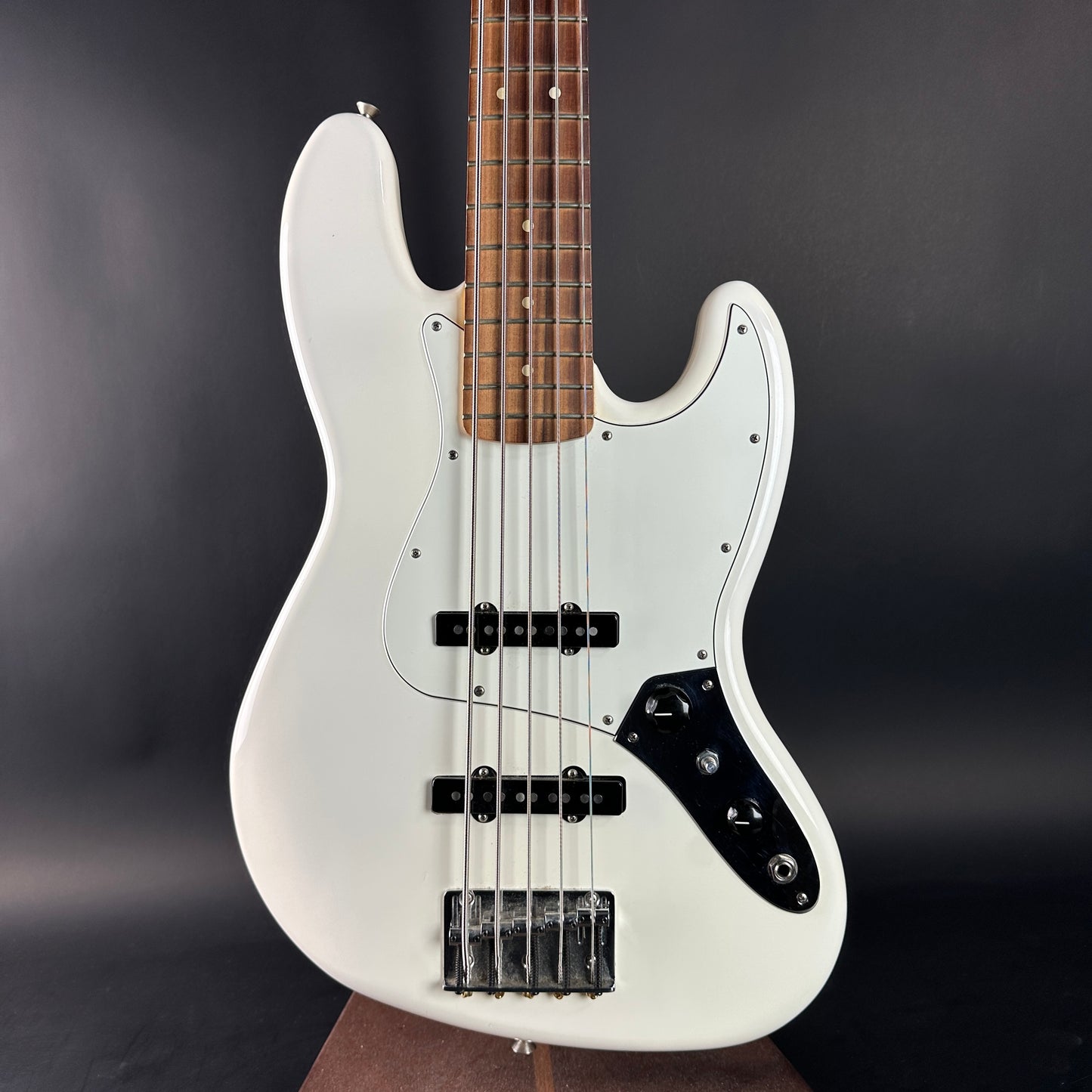 White electric bass guitar with a dark brown neck on a black background