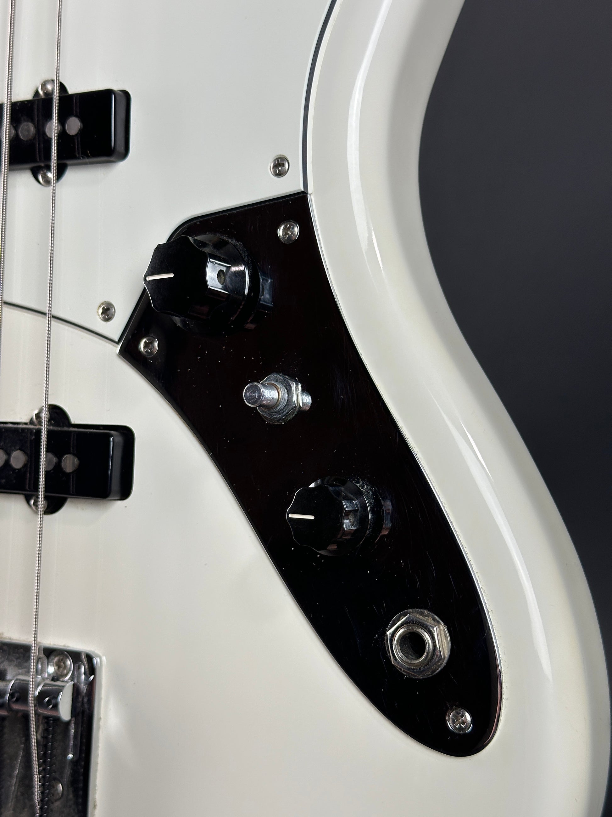Close-up of a white electric bass guitar with a black pickguard on a dark background
