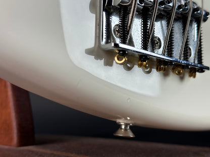 Close-up of a guitar's bridge and tuning pegs on a white guitar body.