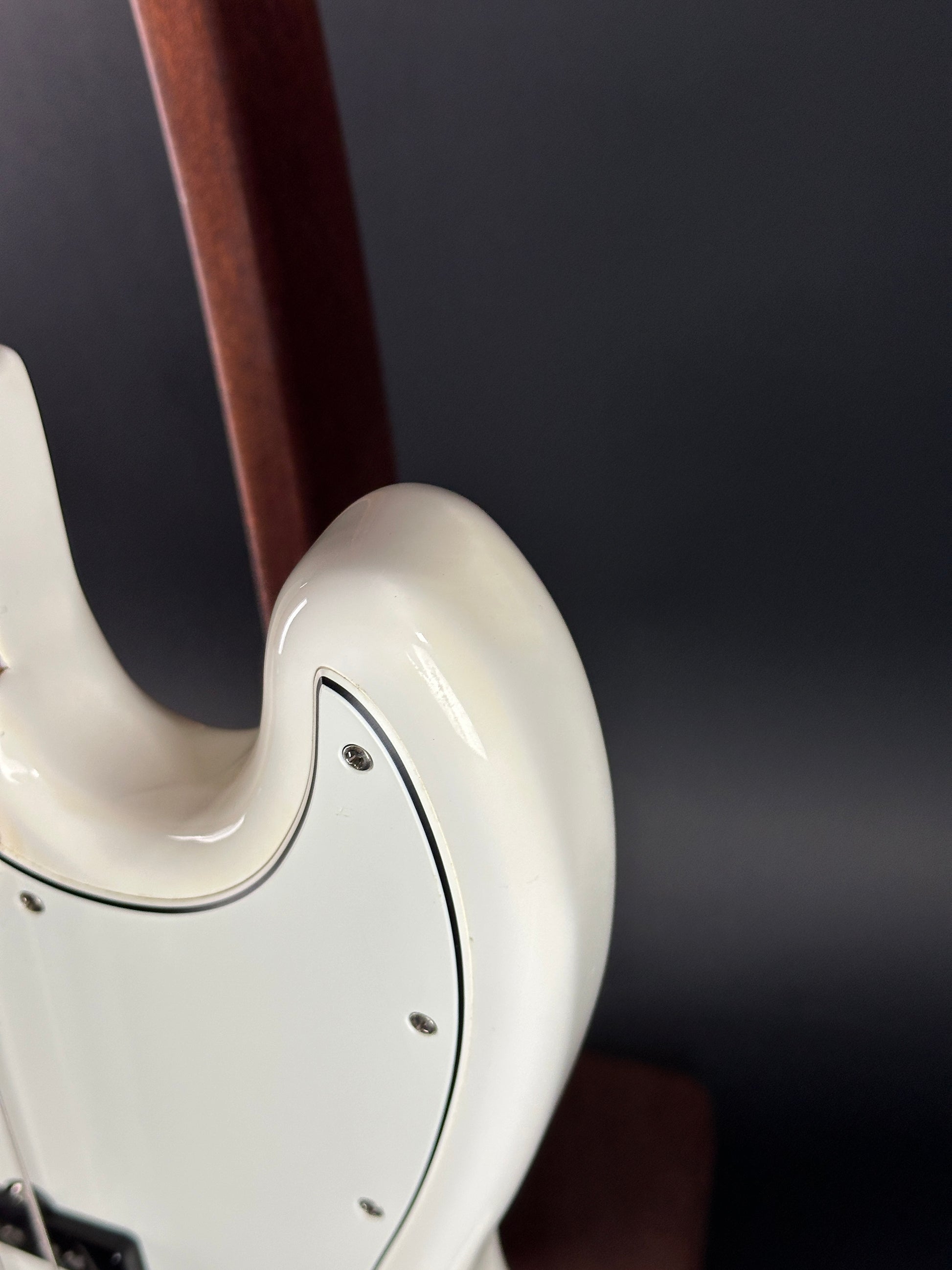 Close-up of a white guitar neck and headstock against a dark background