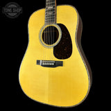 A close-up studio shot of the front and upper body of an acoustic guitar against a solid black background. The guitar has a bright yellow-gold flamed top, a dark brown pickguard, a black bridge, and a dark fretboard.