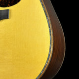 Close-up detail of an acoustic guitar body showing the bright yellow spruce top, a dark brown wood side, and a decorative inlay along the edge against a black background.