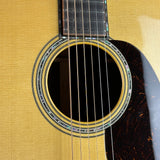 Close-up of an acoustic guitar's sound hole and neck joint, showing the natural wood body, black rosette, strings, and part of the dark tortoiseshell-style headstock.