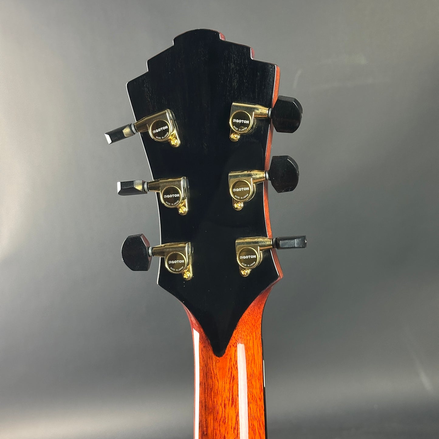 Guitar headstock with tuning pegs on a gray background