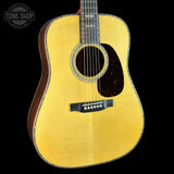 A close-up of a wooden acoustic guitar body with a natural golden-yellow finish, dark brown sides, a black pickguard, and a circular soundhole, shown against a black background with a Tone Shop watermark in the top left.