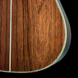 Close-up detail of an acoustic guitar's wooden body, showing a rich brown wood grain finish with a decorative inlay running along the edge against a black background.