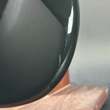 Close-up of a glossy dark green ceramic bowl resting on a wooden surface against a neutral gray background.