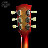 Close-up of the headstock of a guitar, showing six white tuning pegs and a red-to-gold gradient finish against a black background. A Tone Shop watermark is visible in the top left corner.