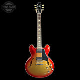 An electric guitar with a red-to-brown sunburst finish, shown against a solid black background. The brand 'Gibson' is visible on the headstock.