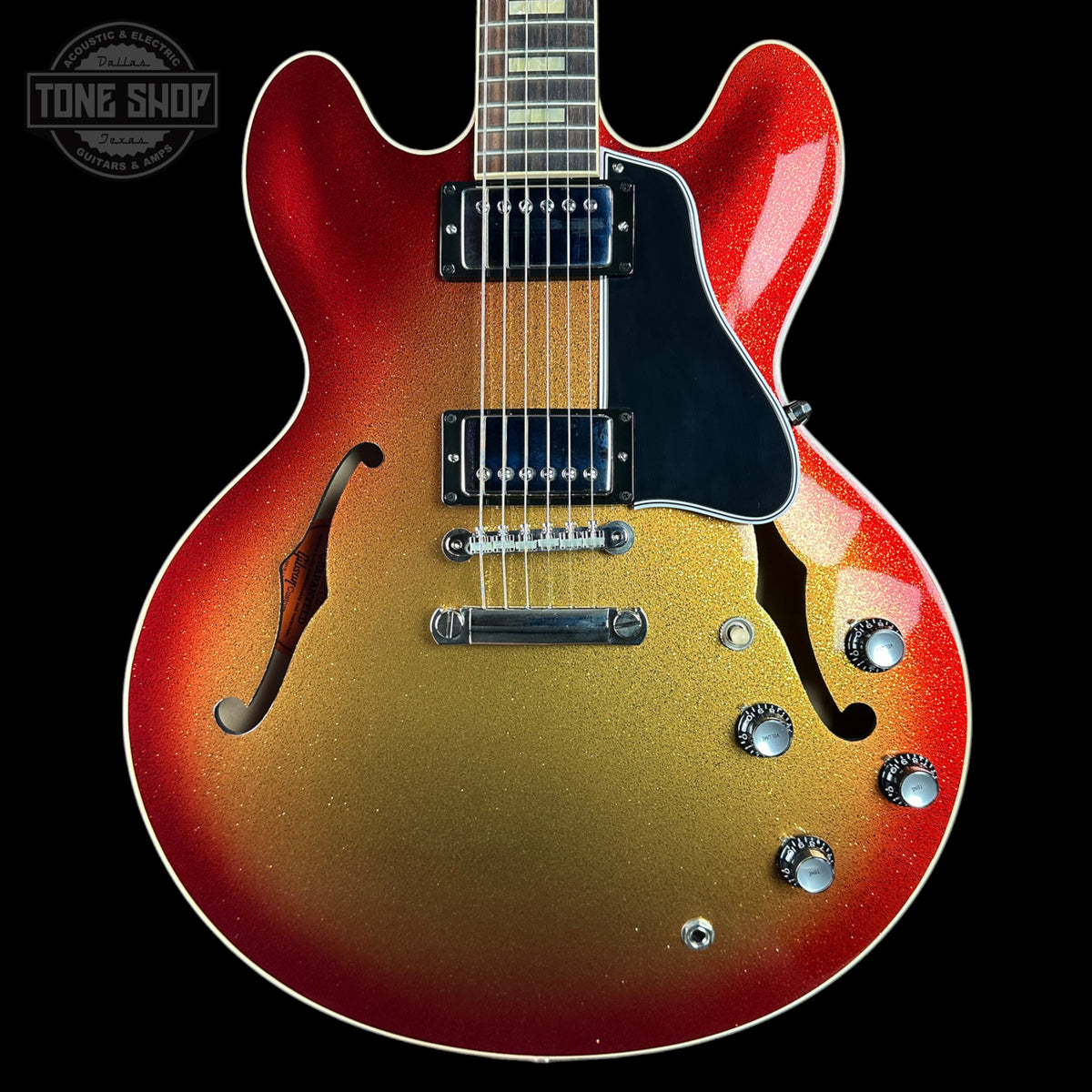 A double-cutaway electric guitar with a red-to-gold-to-brown sunburst finish, featuring a black pickguard and chrome hardware, shown against a solid black background.