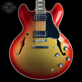 A double-cutaway electric guitar with a red-to-gold-to-brown sunburst finish, featuring a black pickguard and chrome hardware, shown against a solid black background.